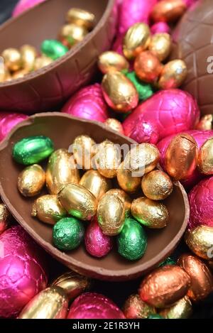 Pile or group of multi coloured & different sizes of colourful foil wrapped chocolate easter eggs in pink, red, gold and lime green with two halves. Stock Photo