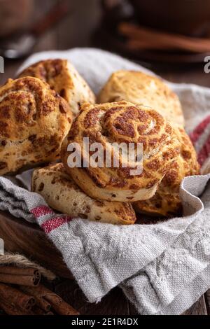 Fresh cinnamon rolls in a bowl and cinnamon sticks on a wooden table Stock Photo