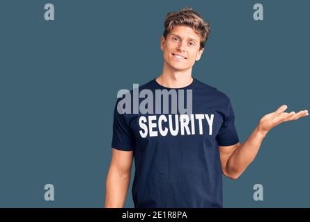 Young handsome man wearing security t shirt smiling cheerful presenting and pointing with palm of hand looking at the camera. Stock Photo