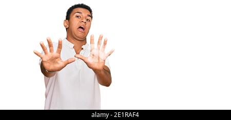 Young arab man wearing casual clothes afraid and terrified with fear expression stop gesture with hands, shouting in shock. panic concept. Stock Photo