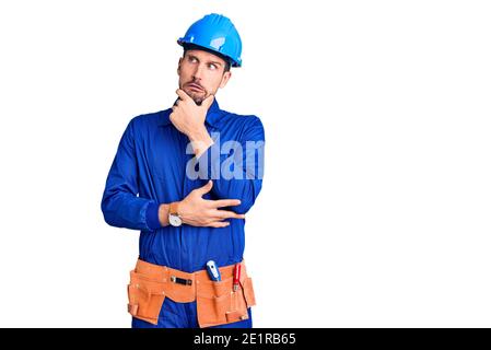 Young handsome man wearing worker uniform and hardhat pointing aside worried and nervous with forefinger, concerned and surprised expression Stock Photo