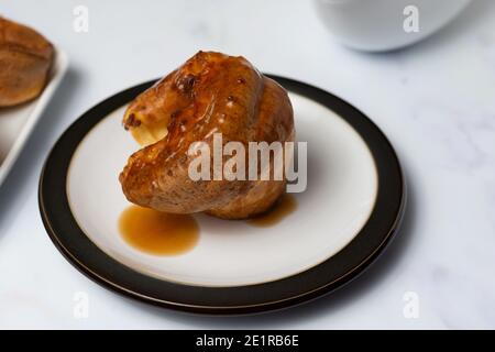 A single Yorkshire pudding covered in gravy sitting on a black rimmed plate on a white background Stock Photo