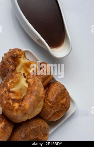 A top down view of a stack of Yorkshire puddings on a white backdrop with a filled gravy boat Stock Photo