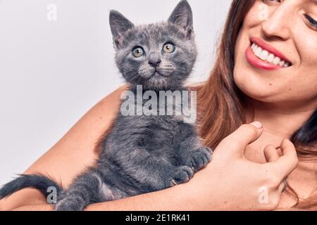 Young beautiful latin woman smilling happy. Standing with smile on face holding adorable cat over isolated white backgroun Stock Photo