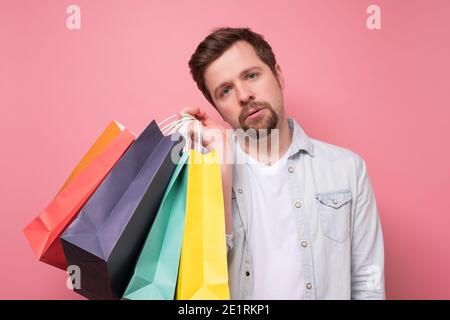 Tired caucasian guy holding a shopping bags. Studio shot on pink wall. Stock Photo