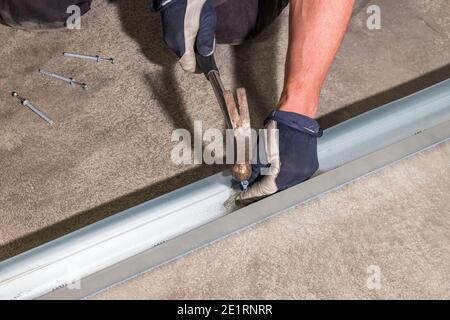 View of male worker hammering dowel nails in metal rail. Construction concept. Stock Photo