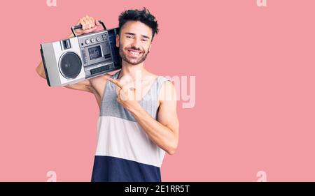 Young hispanic man holding boombox, listening to music smiling happy pointing with hand and finger Stock Photo