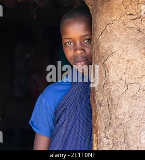 Lake Eyasi, Arusha, Tanzania - 03 October 2020: Young girl being shy and hiding partially inside her house Stock Photo