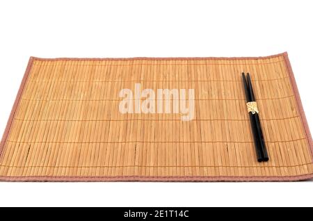 Bamboo food mat with black chopsticks isolated on white background. Traditional kitchen utensils. Stock Photo