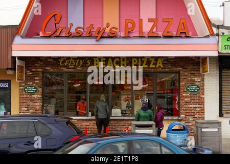 Salisbury Beach, Massachusetts - A brightly colored pizza shop on the boardwalk with the server and customers wearing masks and winter outerwear on an Stock Photo
