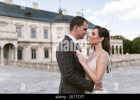 Bride and groom embracing and looking at each other in the background of palace Stock Photo