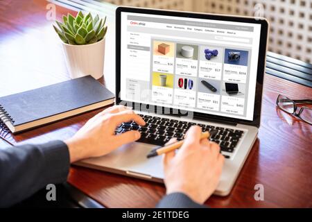 Online shop eshop website developer, Man working with a computer laptop, ecommerce web page on the screen, office desk background. Stock Photo