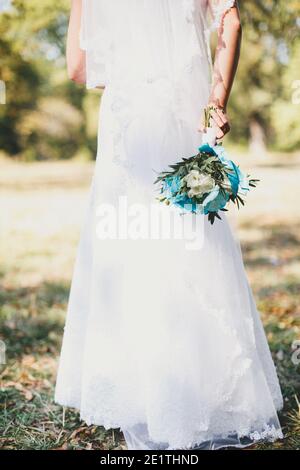 Bride in white dress is holding wedding bouquet. Blurred background Stock Photo