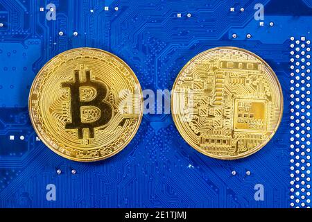 Virtual cryptocurrency money Bitcoin golden coins on a computer printed circuit board PCB. The future of money. Computational equipment. Blue mother b Stock Photo