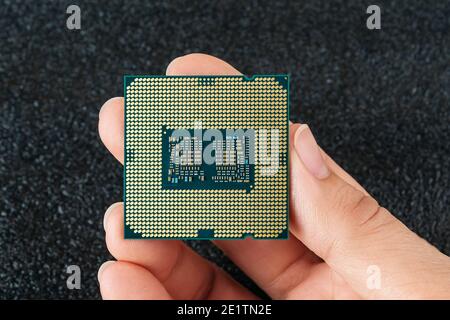 Woman fingers hold pc micro CPU with gold plated contacts against dark background. Modern central processing unit close-up. Desktop computer hardware Stock Photo