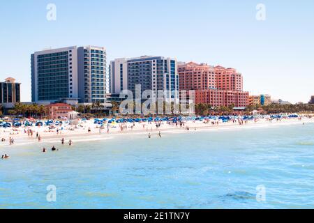 Tropical sandy beach vacation city Clearwater Beach in Florida, colourful beachfront hotel resorts buildings, sea and sunbathing tourists Stock Photo