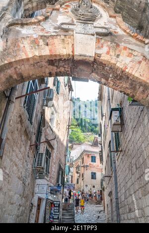 Visitors to the Old Town walk along a narrow street underneath the arch of an ancient stone gateway leading up to the surrounding mountains. Stock Photo