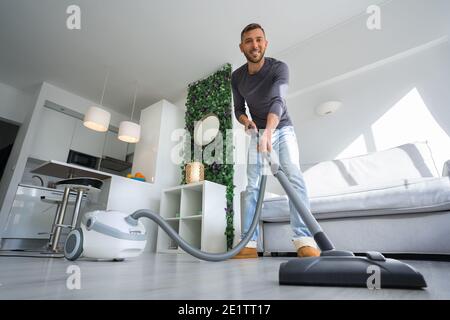 Young attractive man using a vacuum cleaner at home. Man cleaning house. House keeping concept Stock Photo