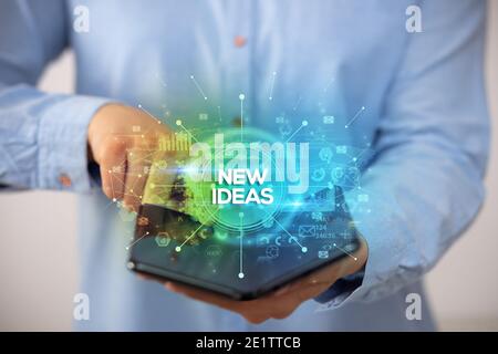 Businessman holding a foldable smartphone with NEW IDEAS inscription, new business concept