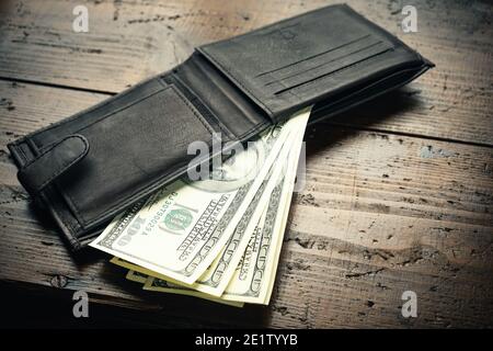 Leather wallet full of money on wooden table - one hundred US banknotes with president Franklin portrait. Cash of hundred dollar bills, paper currency Stock Photo