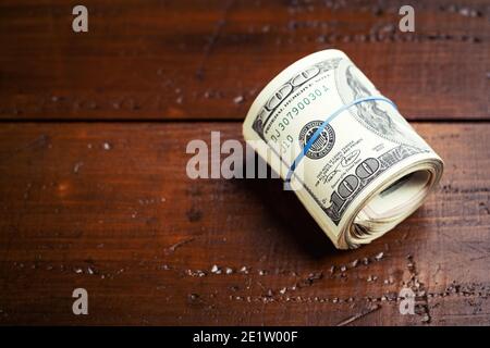 Roll of money with rubber on wooden table - one hundred US banknotes with president Franklin portrait. Cash of hundred dollar bills, paper currency ba Stock Photo