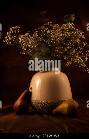 Soft white vase with 'baby's breath' flowers on a dark background,  Artificial fruit adds a nice accent. Stock Photo
