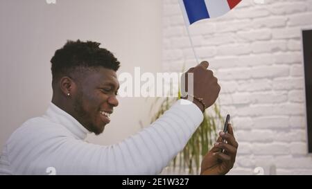 Black man having a video call or watching a game on smartphone while waving flag of France. High quality photo Stock Photo