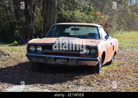 A neglected 1970 Plymouth Roadrunner in faded Vitamin C orange paint sits in a yard. Stock Photo