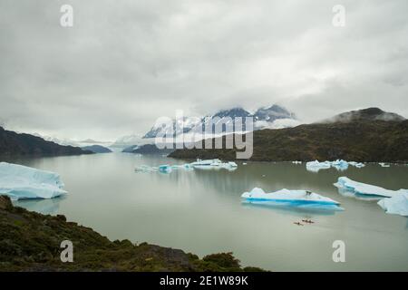 Tourists in kayaks on Lago Grey dwarfed by icebergs calved from Glacier Grey and the mountain landscape, Torres del Paine, Patagonia, Chile Stock Photo