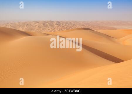 Man in traditional omani outfit sitting over a sand dune in the arabian desert Stock Photo