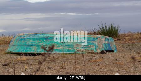 The old inverted green color boat lies on the sea shore in cloudy day. Stock Photo