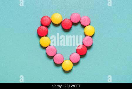 Flat lay with multi-colored macarons arranged in a heart shape on a green background. Delicious homemade macaroons. Stock Photo