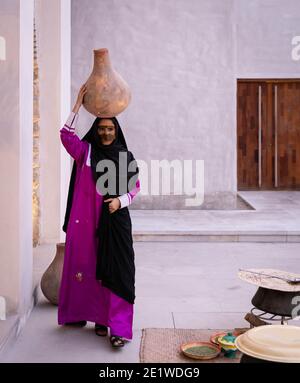 Emarati lady in traditional clothes holding a jar over her head and roaming around the house Stock Photo