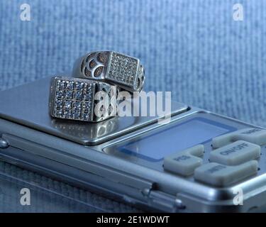 Close up shot of a pair of silver rings studded with zirconium stones for men and women, on top of an electronic weighing scale. Stock Photo