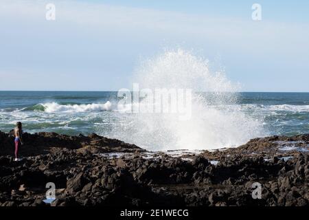 A woman watching a large wave crashing onto the rocky shore near Yachats, Oregon. Stock Photo
