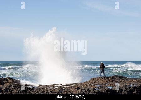 A huge wave crashing very close to a man standing on the rocky shore near Yachats, Oregon. Stock Photo