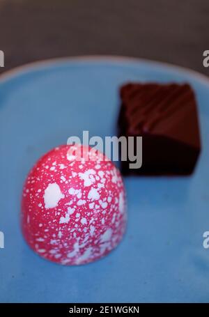 Closeup of Pink and White Colored White Chocolate Bonbon with Blurry Dark Chocolate Bonbon in Background Stock Photo