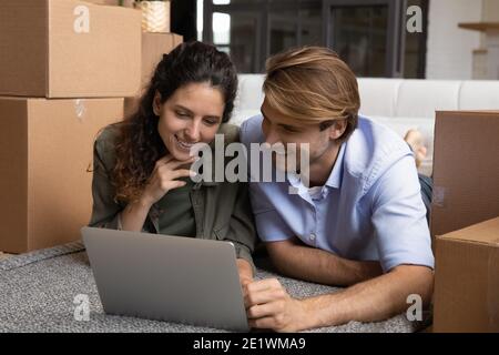 Happy couple lying on floor browsing laptop together Stock Photo