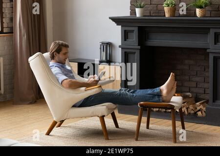 Young Caucasian man relax in chair using tablet Stock Photo
