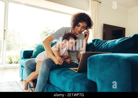 Woman on a business call working from home. Working mother talking on mobile phone with baby on sofa Stock Photo