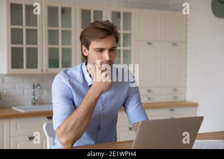 Pensive young man look at laptop screen thinking Stock Photo