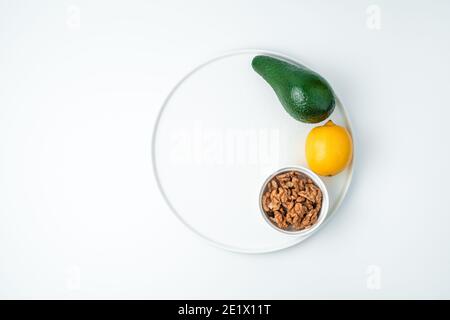 Avocado, lemon and walnuts in a plate on a white background. Stock Photo