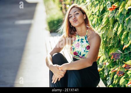 Pretty young girl sitting on urban bench blowing a kiss Stock Photo