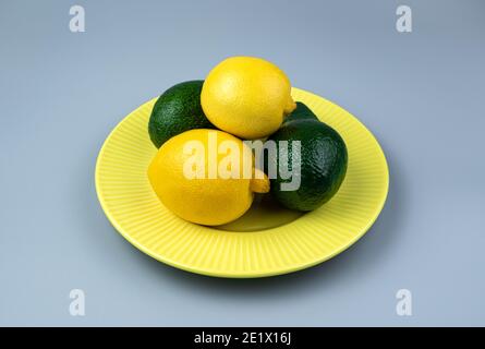 Fresh lemons and avocados in a yellow plate on a gray background. Side view with space to copy. Stock Photo