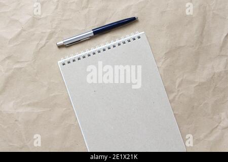 Gray notepad with white coiled spring and pen on a background of beige crumpled craft paper. With empty space for text and design Stock Photo