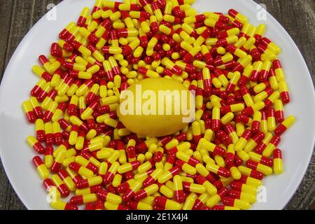Close up of one ripe raw lemon on medical colorful yellow red capsules and white plate - Vitamin c supplement concept (focus on center) Stock Photo