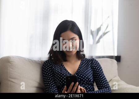 Smiling vietnamese asian woman using smartphone at home. Stock Photo