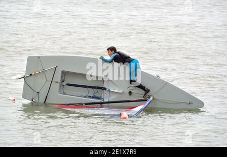 Capsized Sailing Dinghy with young man trying  to right it, in the sea at Felixstowe Suffolk England. Stock Photo