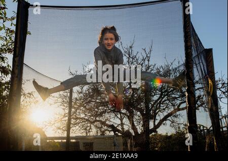 Edinburgh, Scotland, UK. January 2021. A 14 year old girl jumping on a back garden trampoline as the sun sets in winter Stock Photo