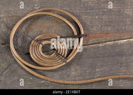 Art leather lace handmade with needle on wood background. Sewing banner. Spiral leather rope. Round lace. Stock Photo